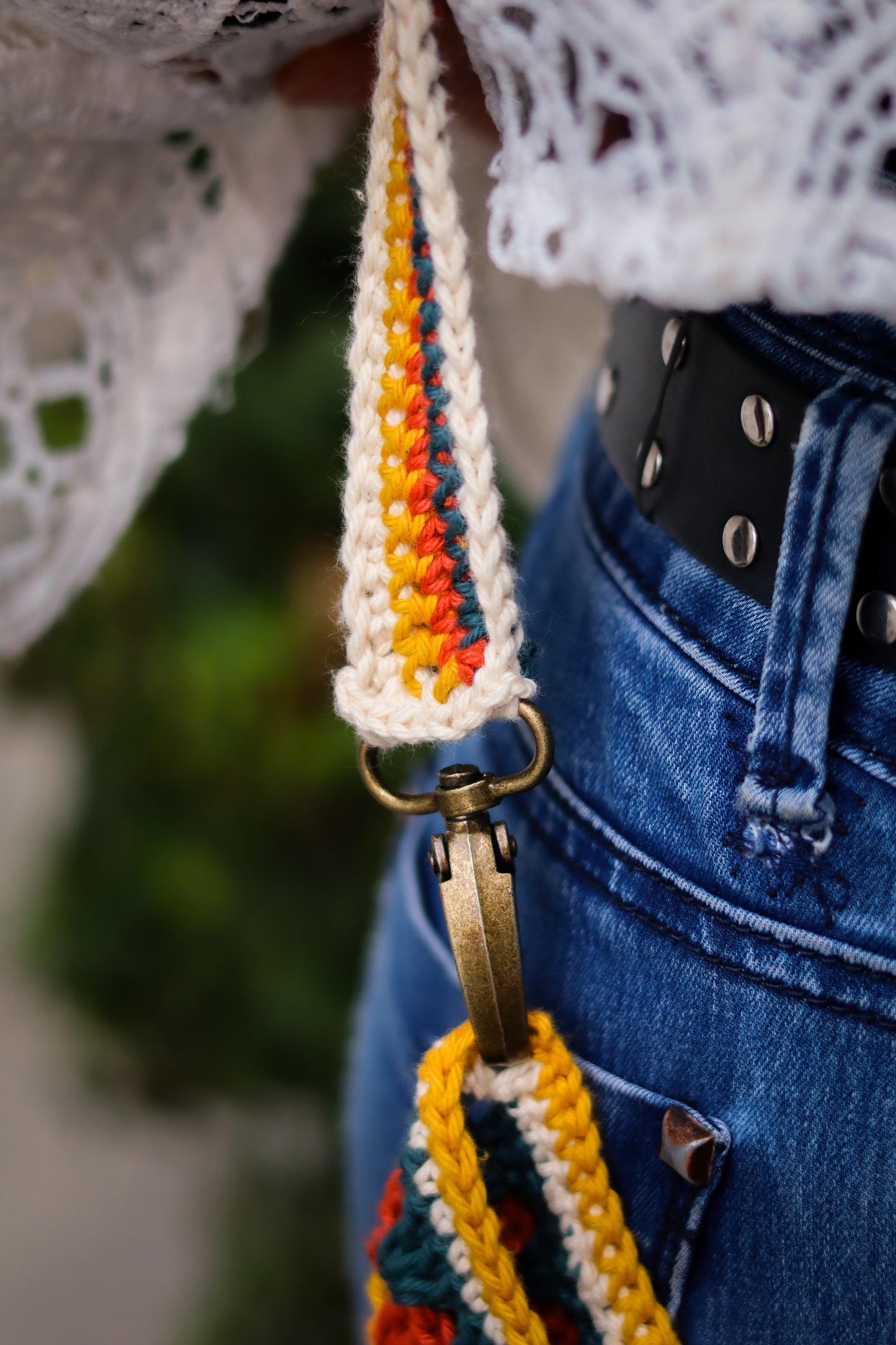Colorful crochet strap hanging from a person wearing a white lace top and blue jeans.