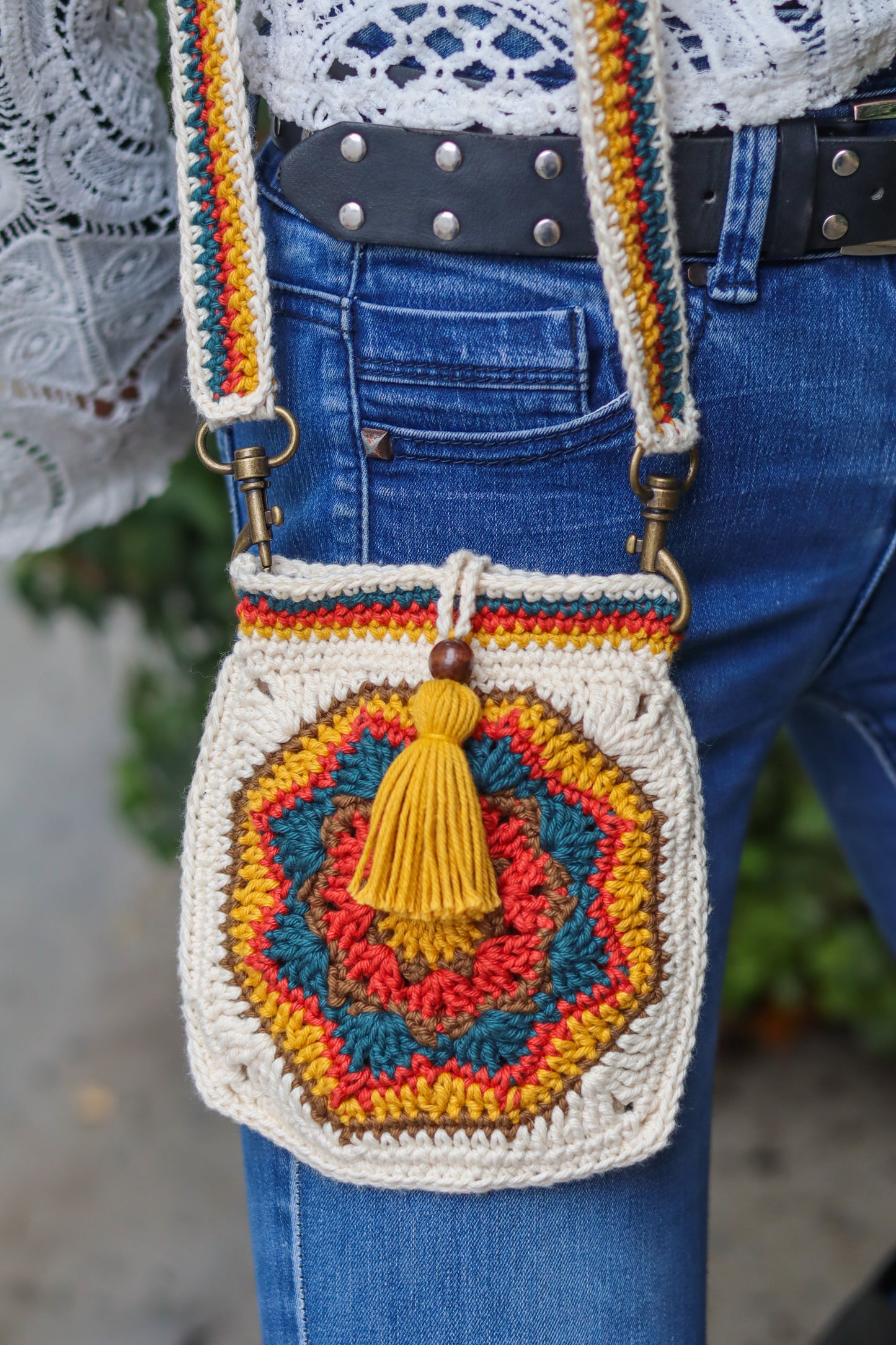 Colorful crochet handbag with a tassel held by a person wearing blue jeans.