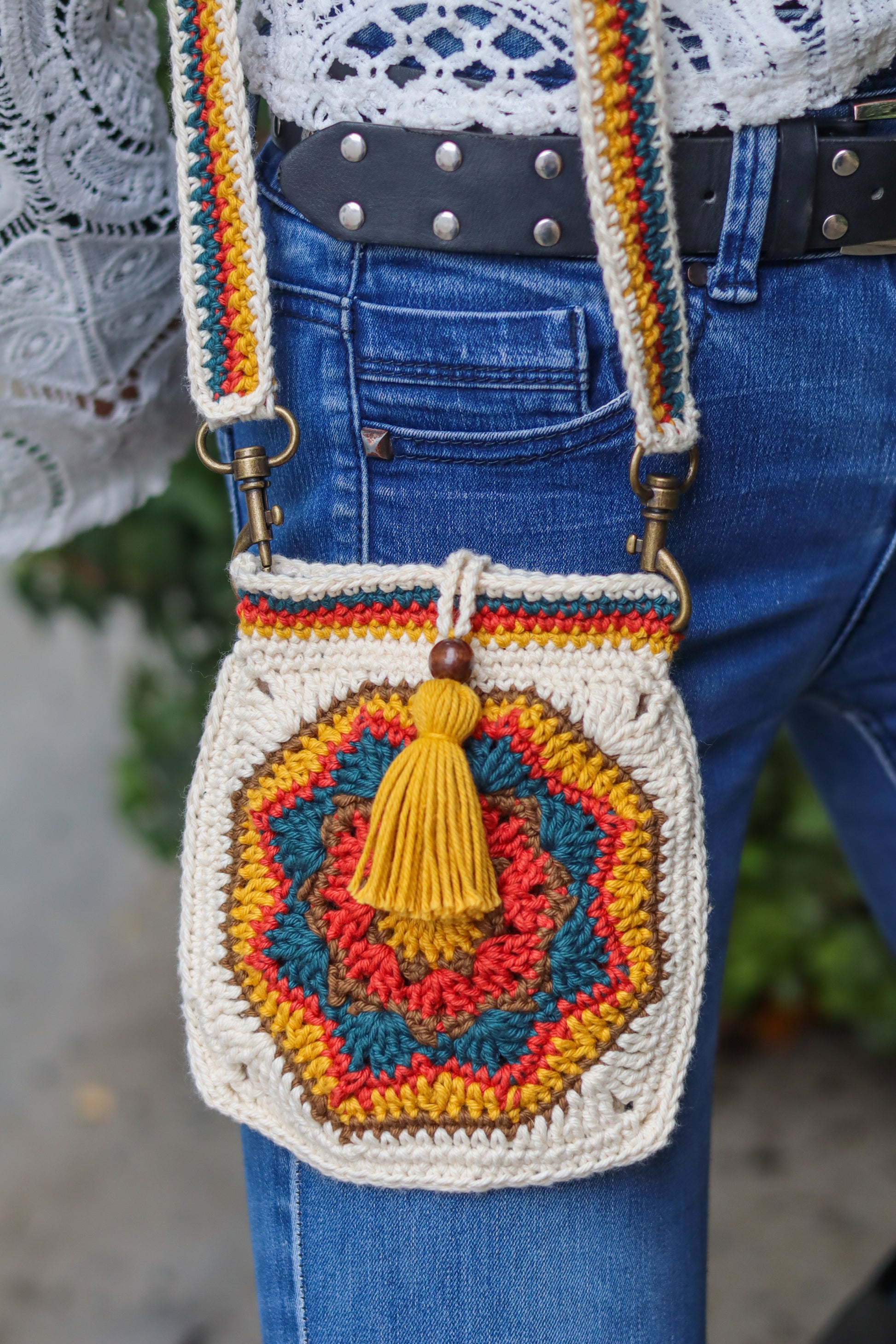 Colorful crochet handbag with a tassel held by a person wearing blue jeans.