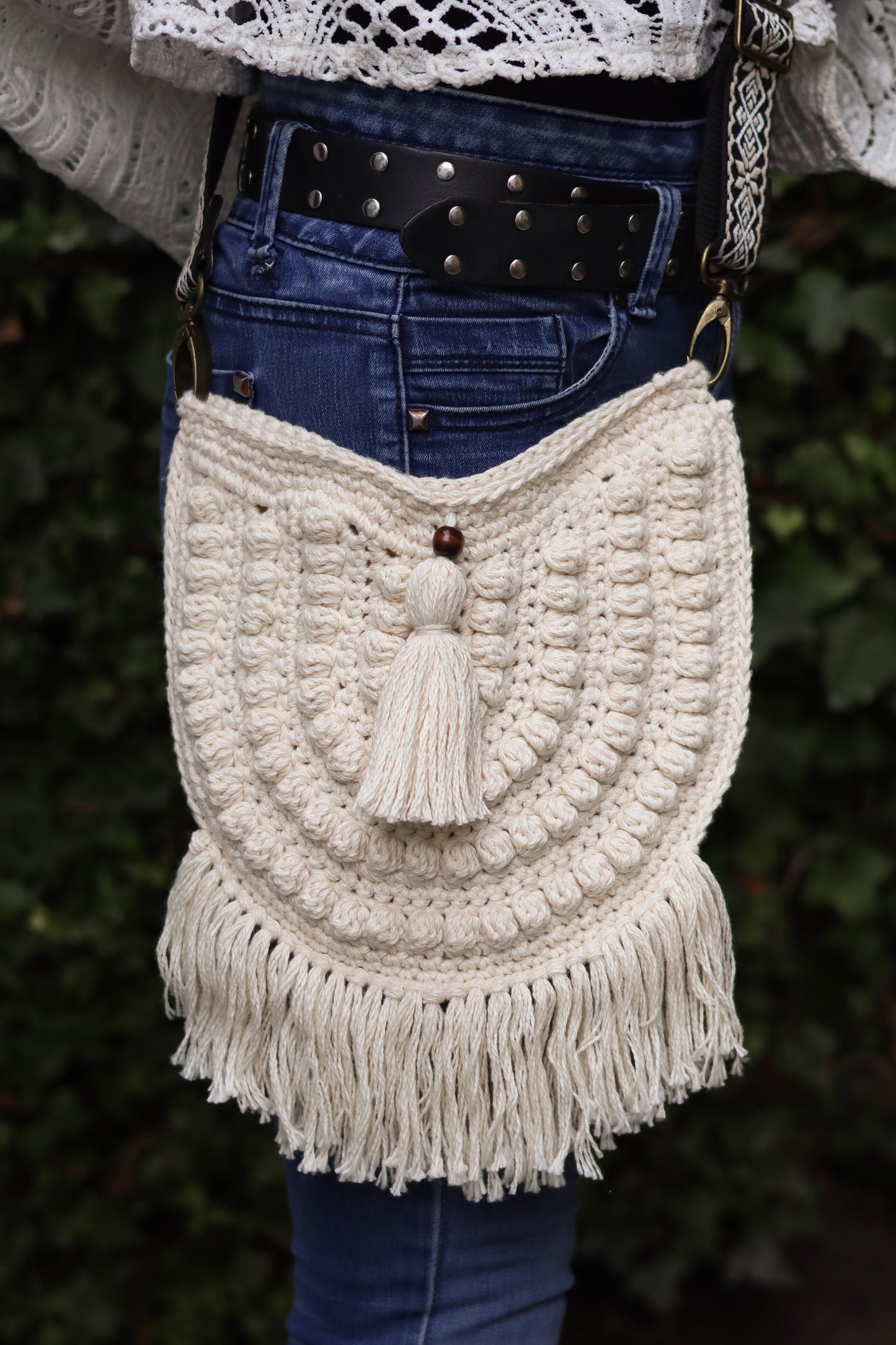 Person wearing a white crochet bag with tassels against a blurred green background