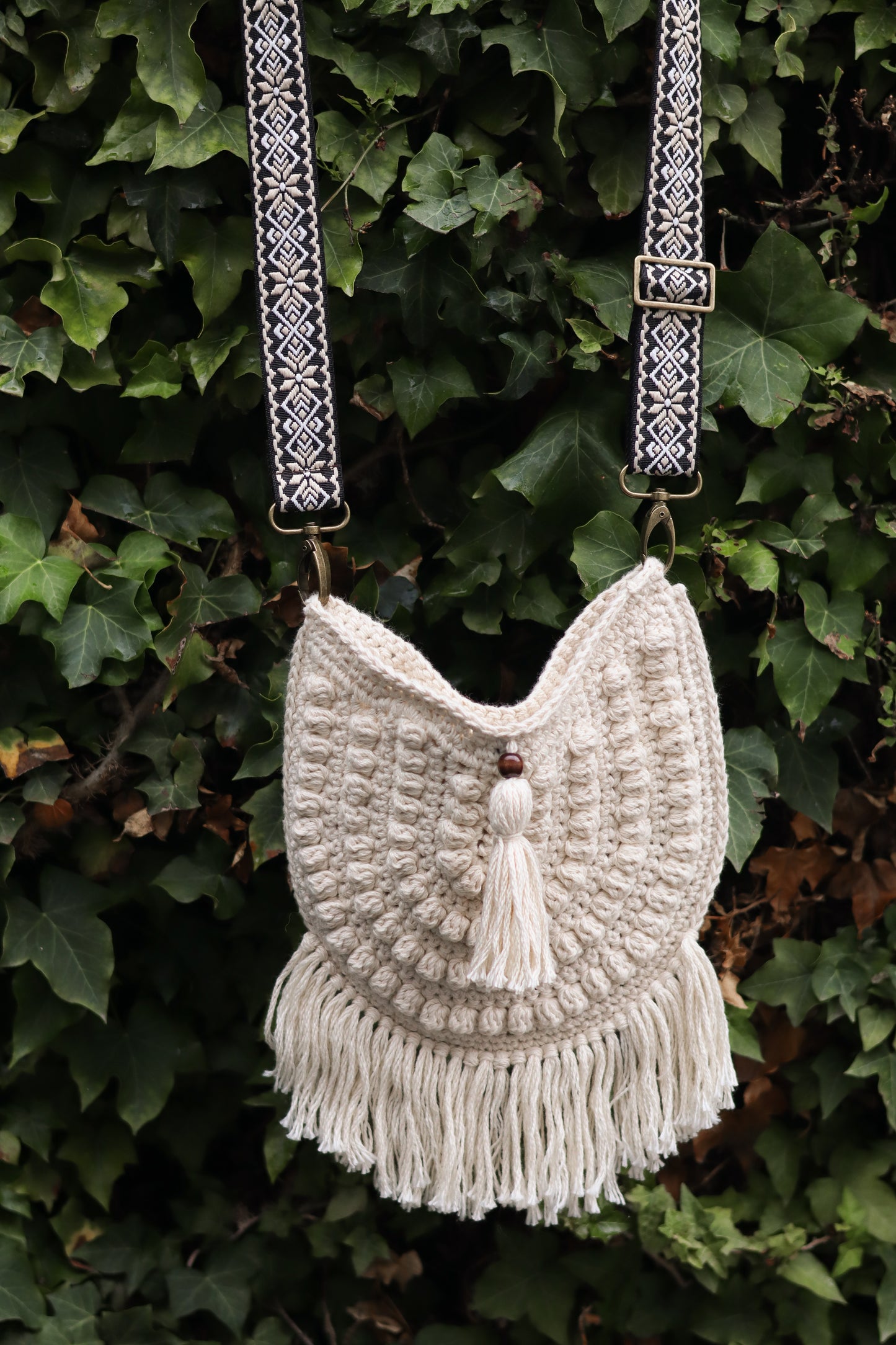 Beige crochet bag with tassel against a green leafy background