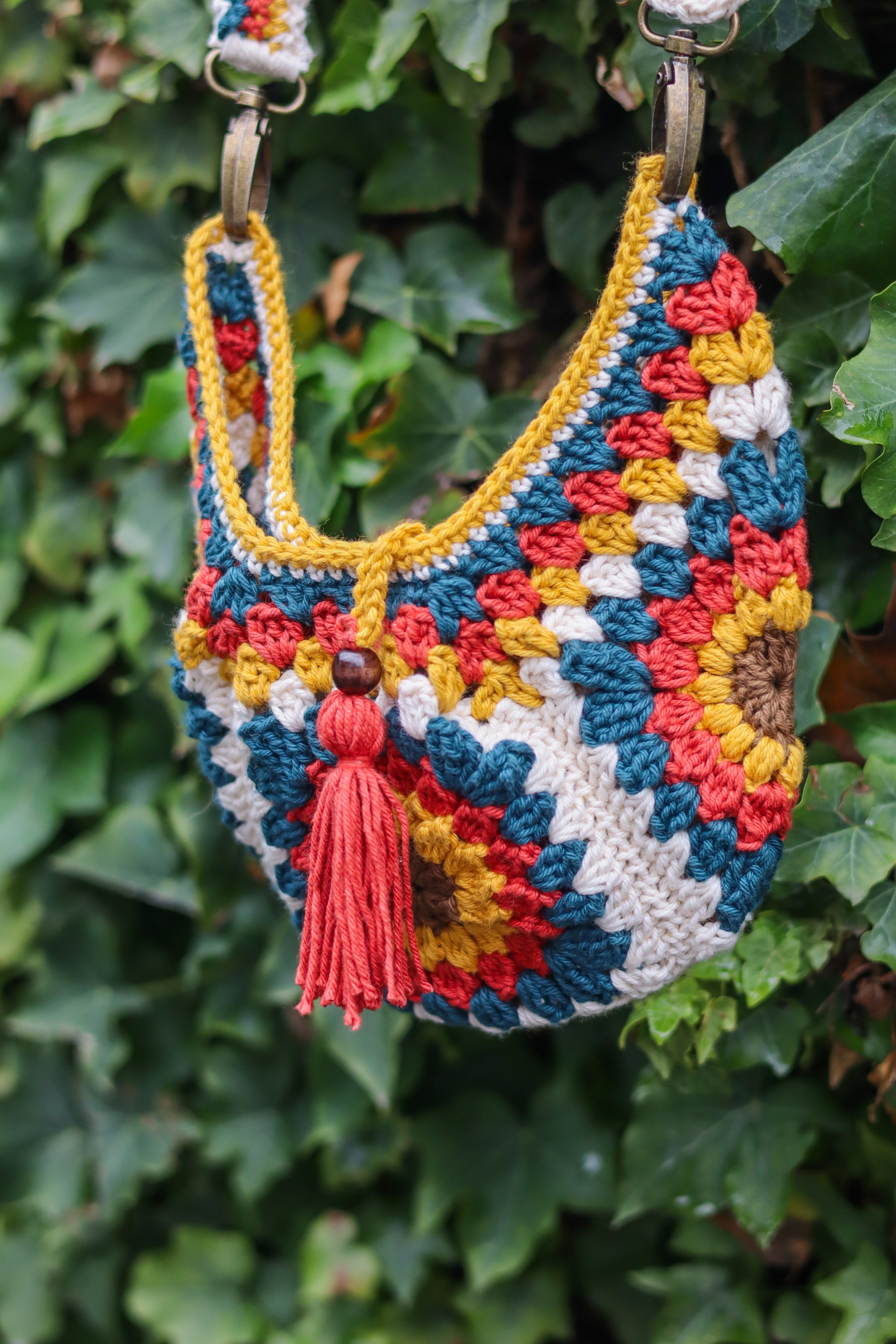 Colorful crocheted handbag with a tassel against a green leafy background