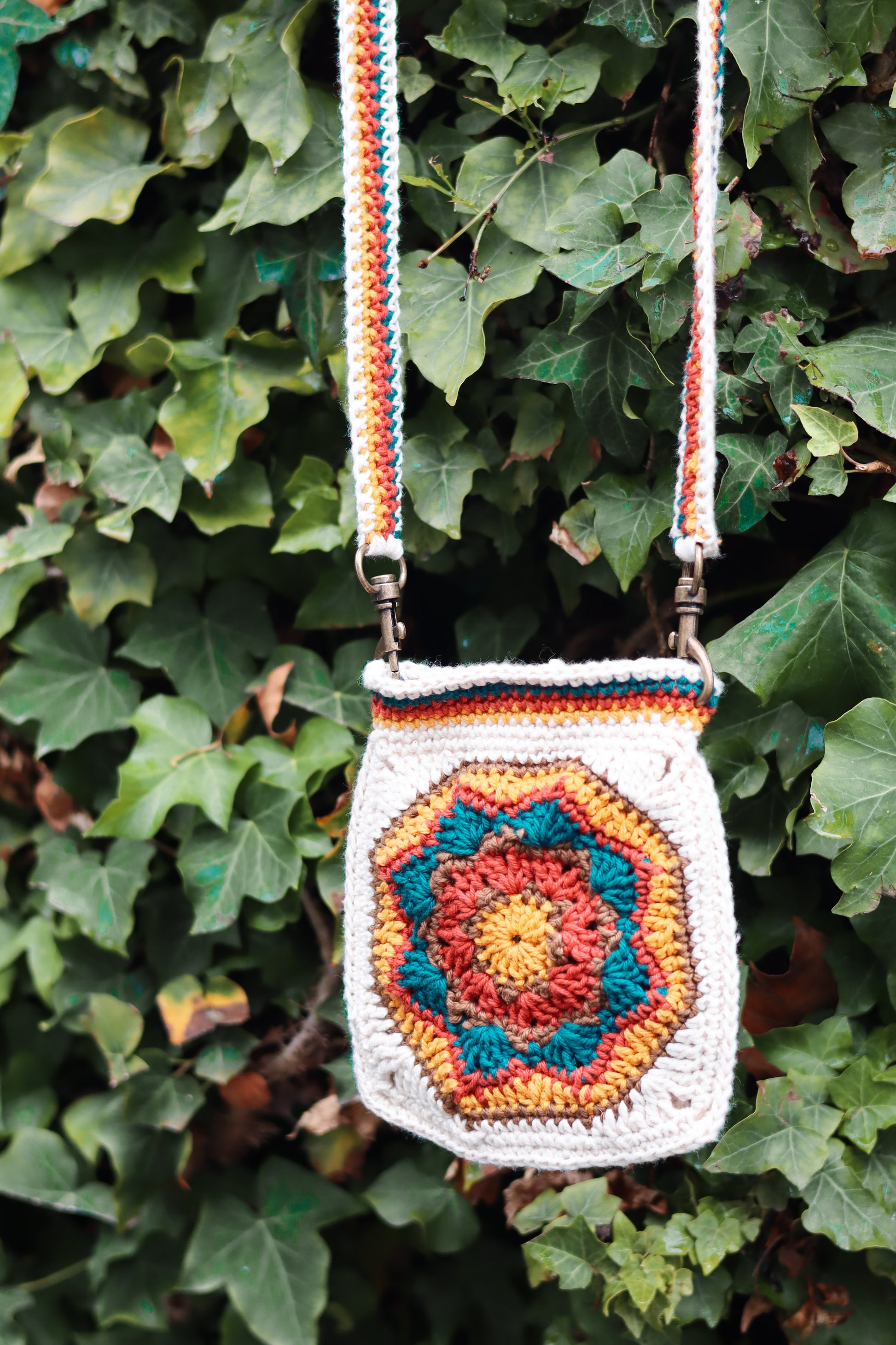 Crocheted bag with colorful pattern against a green leafy background