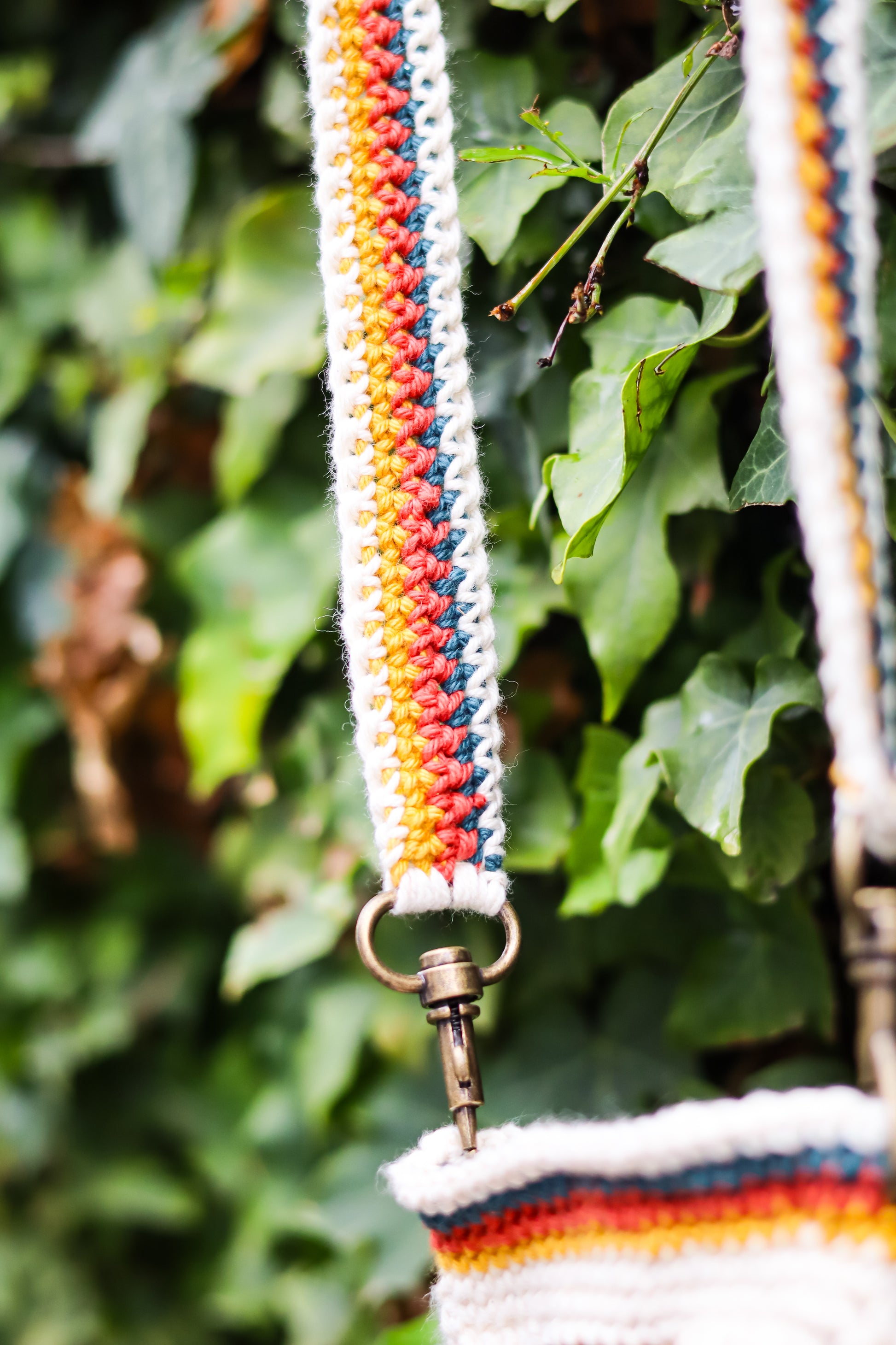 Multicolored striped bag strap with a metal clasp against a green leafy background