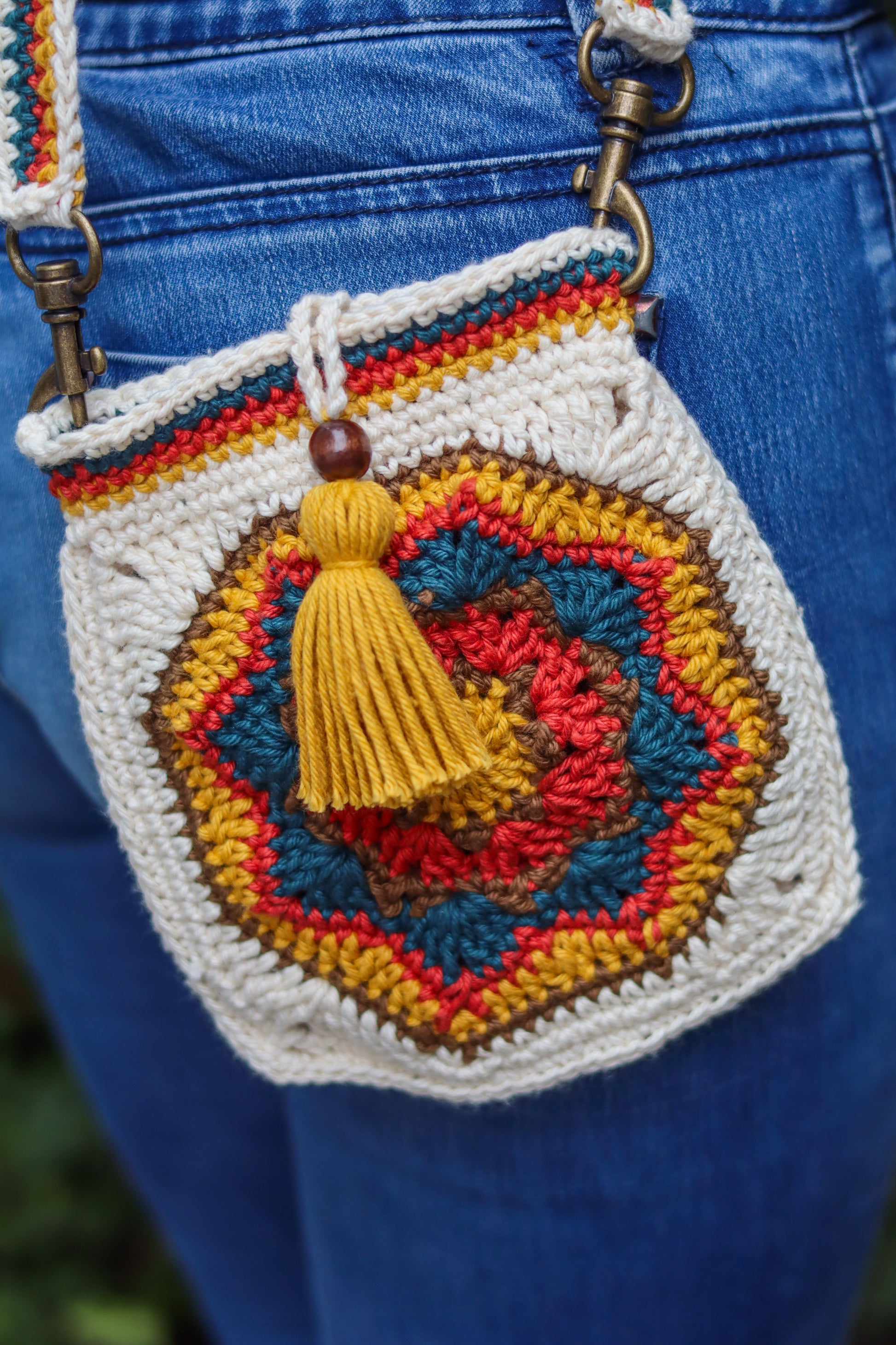 Colorful crochet bag with a tassel on a blue denim background
