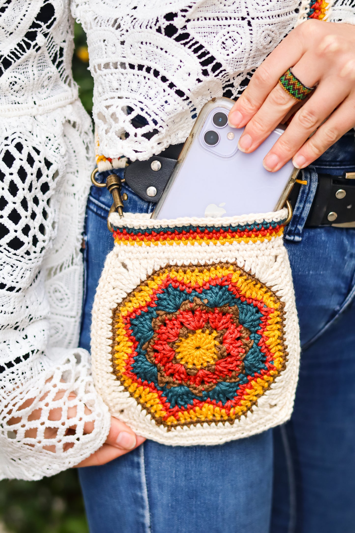Person holding a colorful crochet phone pouch with a patterned design.