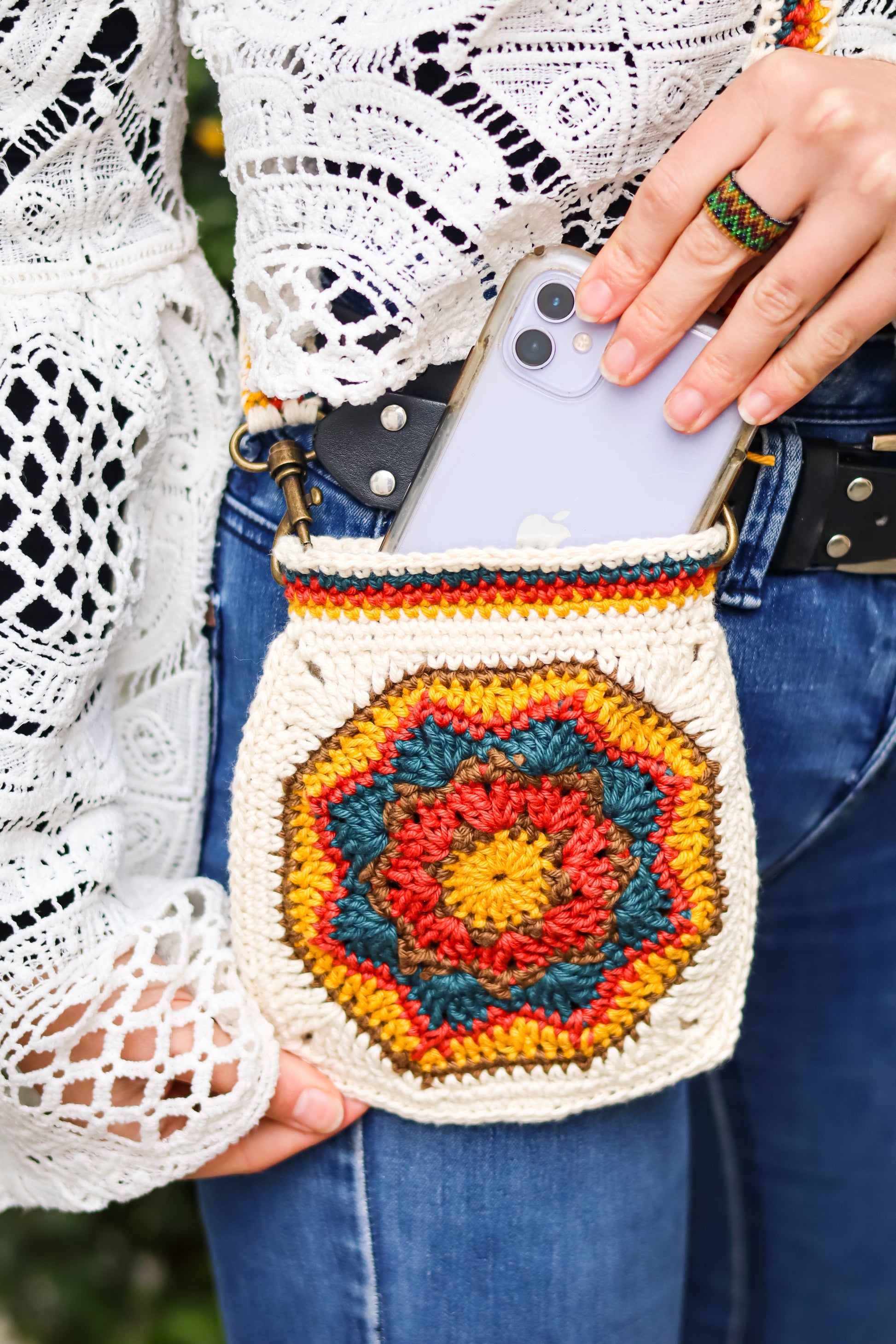 Person holding a colorful crochet phone pouch with a patterned design.