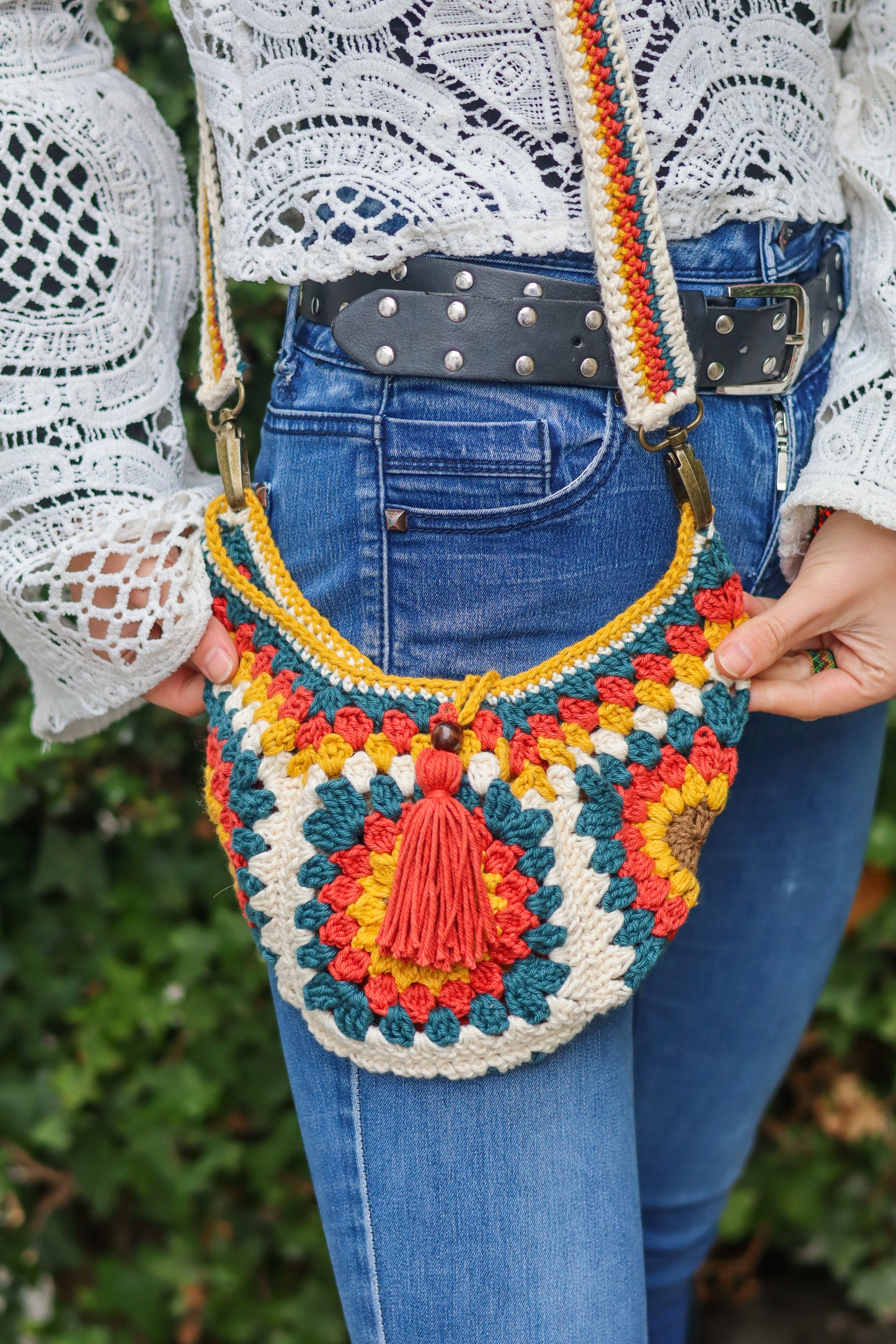 Colorful crocheted bag held by a person wearing blue jeans and a white lace top.